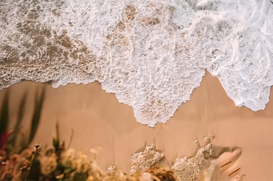 Luchtfoto van zachte golven die het strand raken bij zonsondergang, met schuimend water op goudkleurig zand.