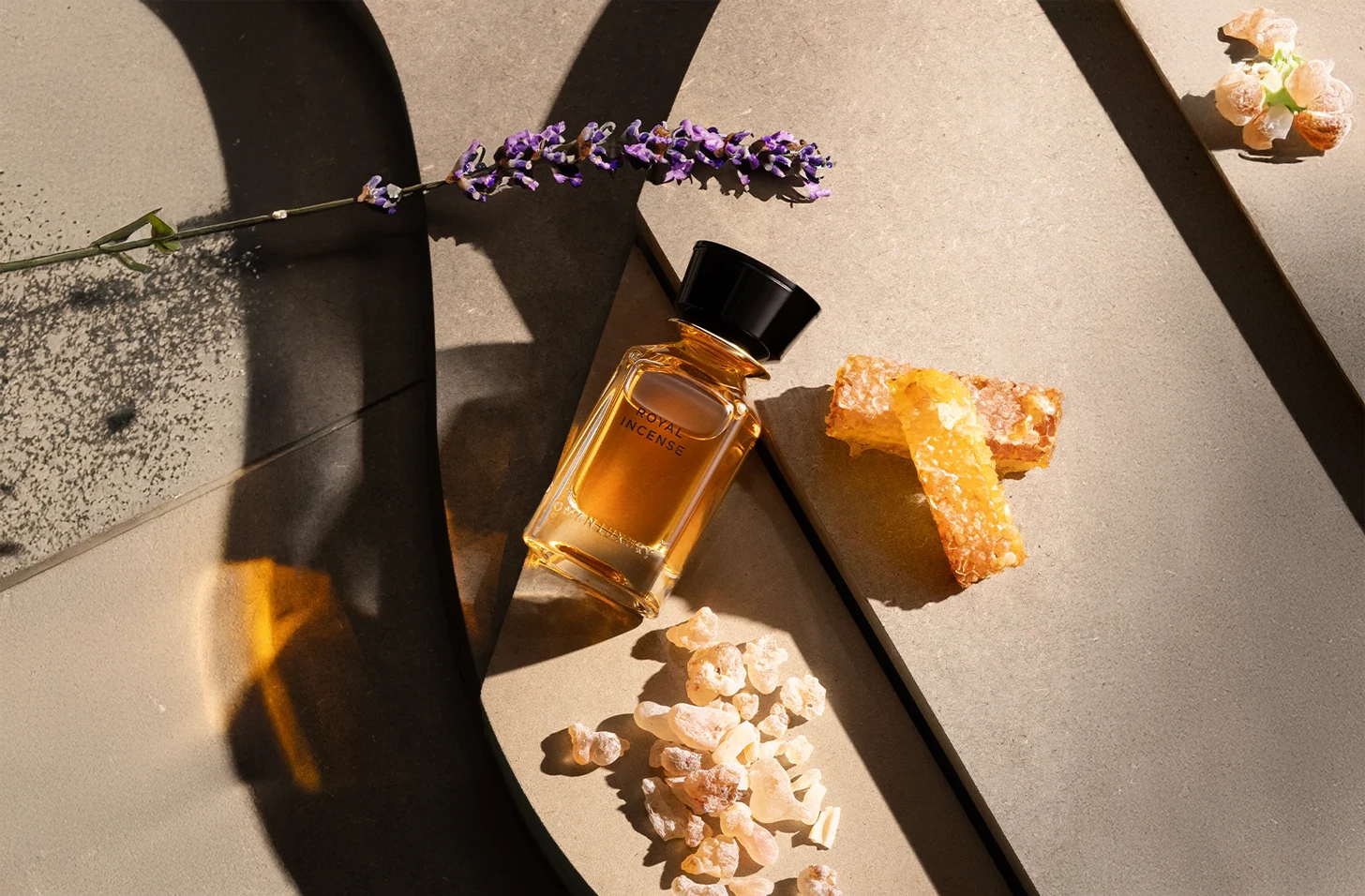 Flacon van Oman Luxury Royal Incense parfum omringd door lavendel, wierookhars en honingraat op een stenen oppervlak met zonlicht en schaduw.