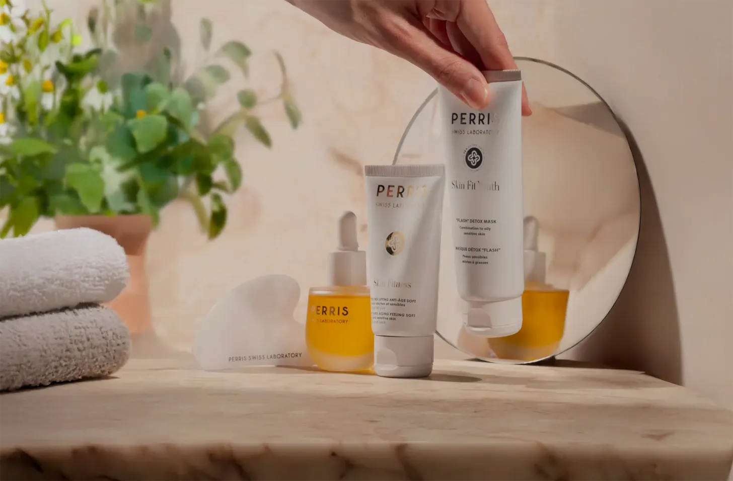 Perris Swiss Laboratory skincare producten op een marmeren wastafel, inclusief serum, crèmes en gua sha steen, met een hand die een detoxmasker vasthoudt.