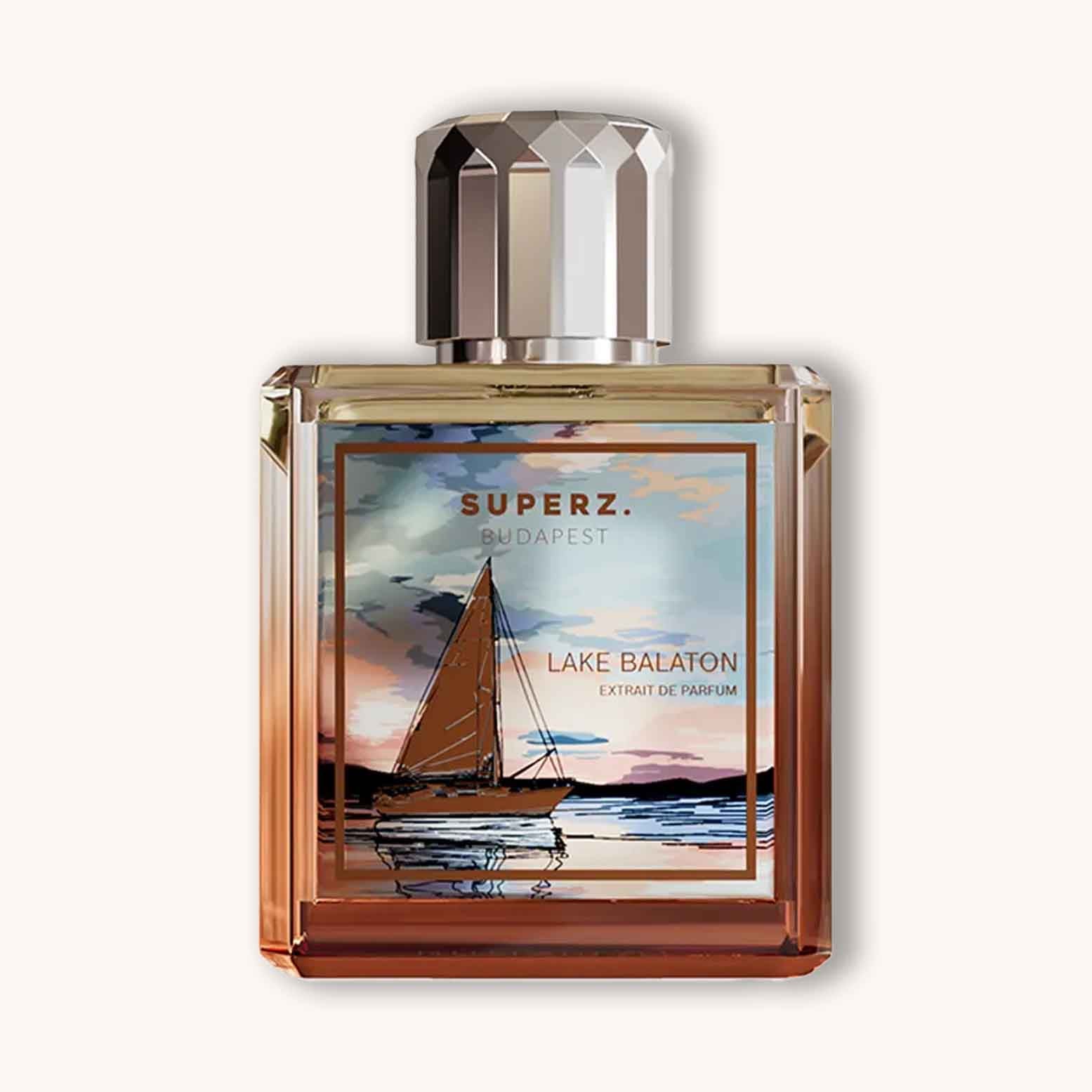 Alt text: A stylish perfume bottle labeled 'Superz Lake Balaton', featuring a picturesque illustration of a sailboat on water at sunset, with warm colors reflecting serenity and nature.